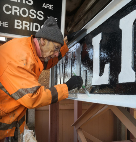 2022.11.29 Chris Hooper refurbishing the  cast iron 'Running In Board'  on Platform 1.  © Richard Salt.